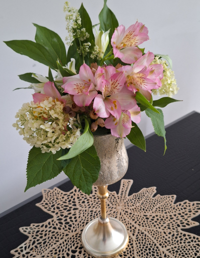 A charming flower arrangement featuring blue hydrangeas, pink roses, and white daisies, accented with greenery in a woven basket.