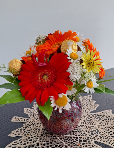 A vibrant bouquet featuring a mix of seasonal flowers in various colors, including sunflowers, roses, and carnations, arranged in a clear glass vase.