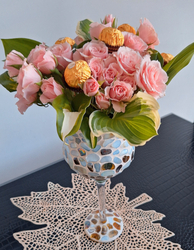 A delicate bouquet of pink and white roses, elegantly arranged with green leaves and baby's breath, displayed in a clear glass vase.