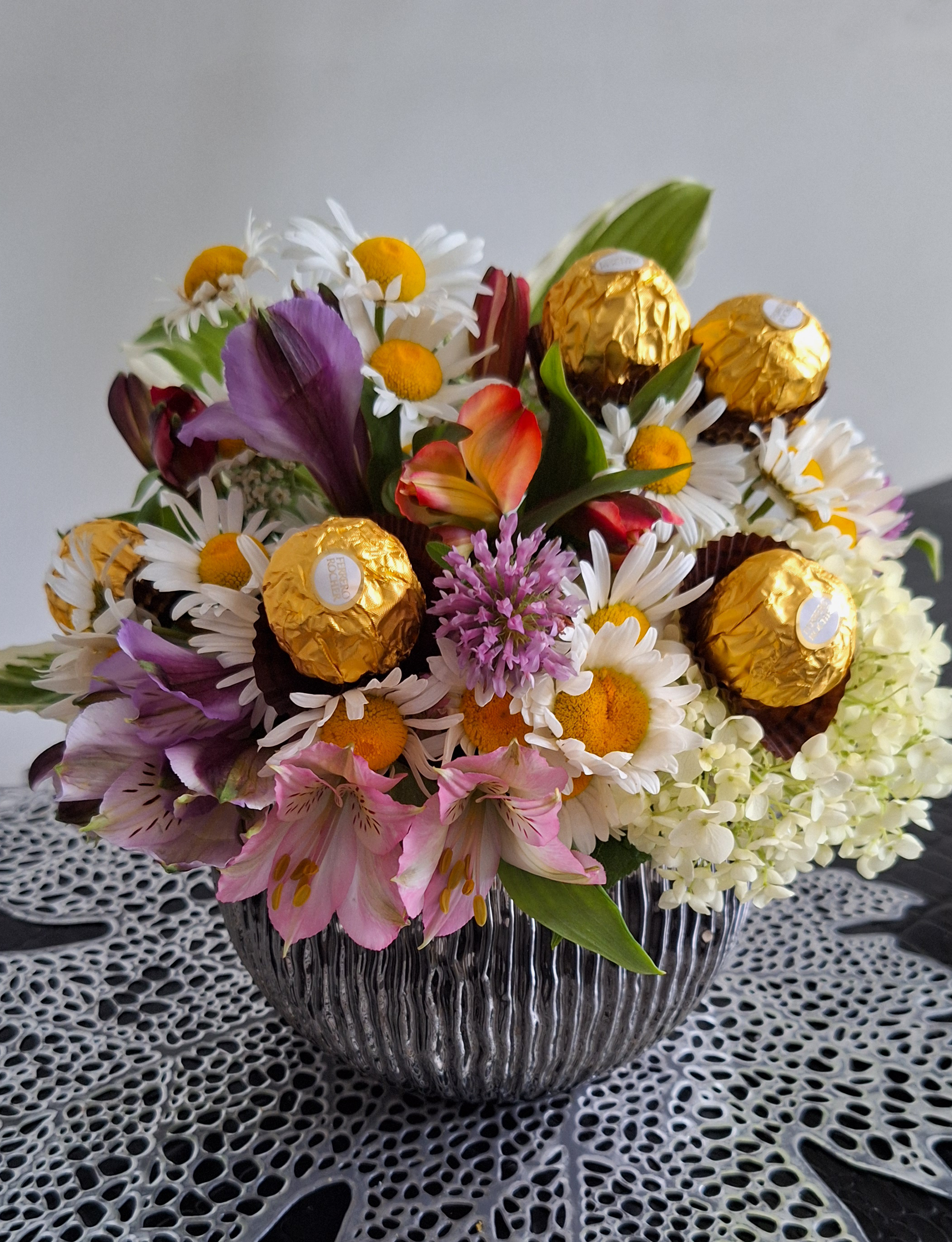 An elegant floral arrangement featuring white roses and green foliage, arranged in a stylish white ceramic pot.