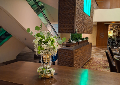 A white and green floral arrangement with crystal accents displayed on a wooden table in a modern hotel lobby, featuring elegant decor and contemporary architecture.