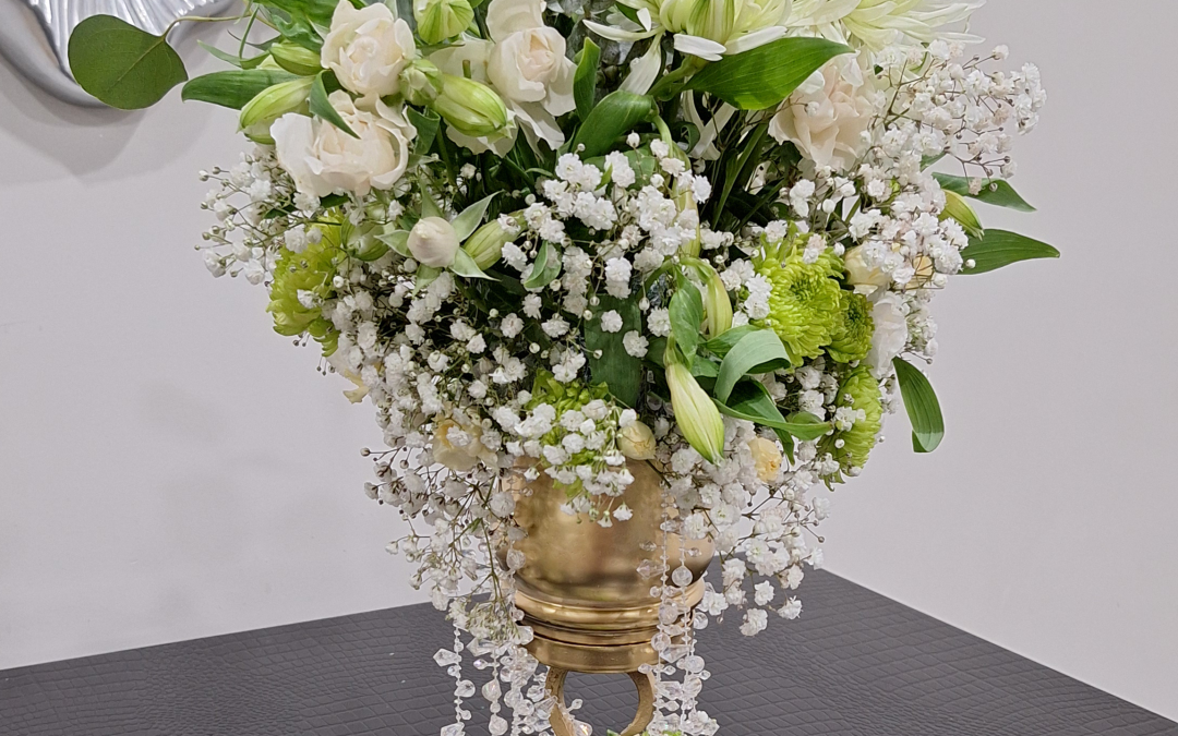 Cascading white and green floral arrangement with roses, chrysanthemums, and eucalyptus in a gold vase with crystal strands and mini vases.