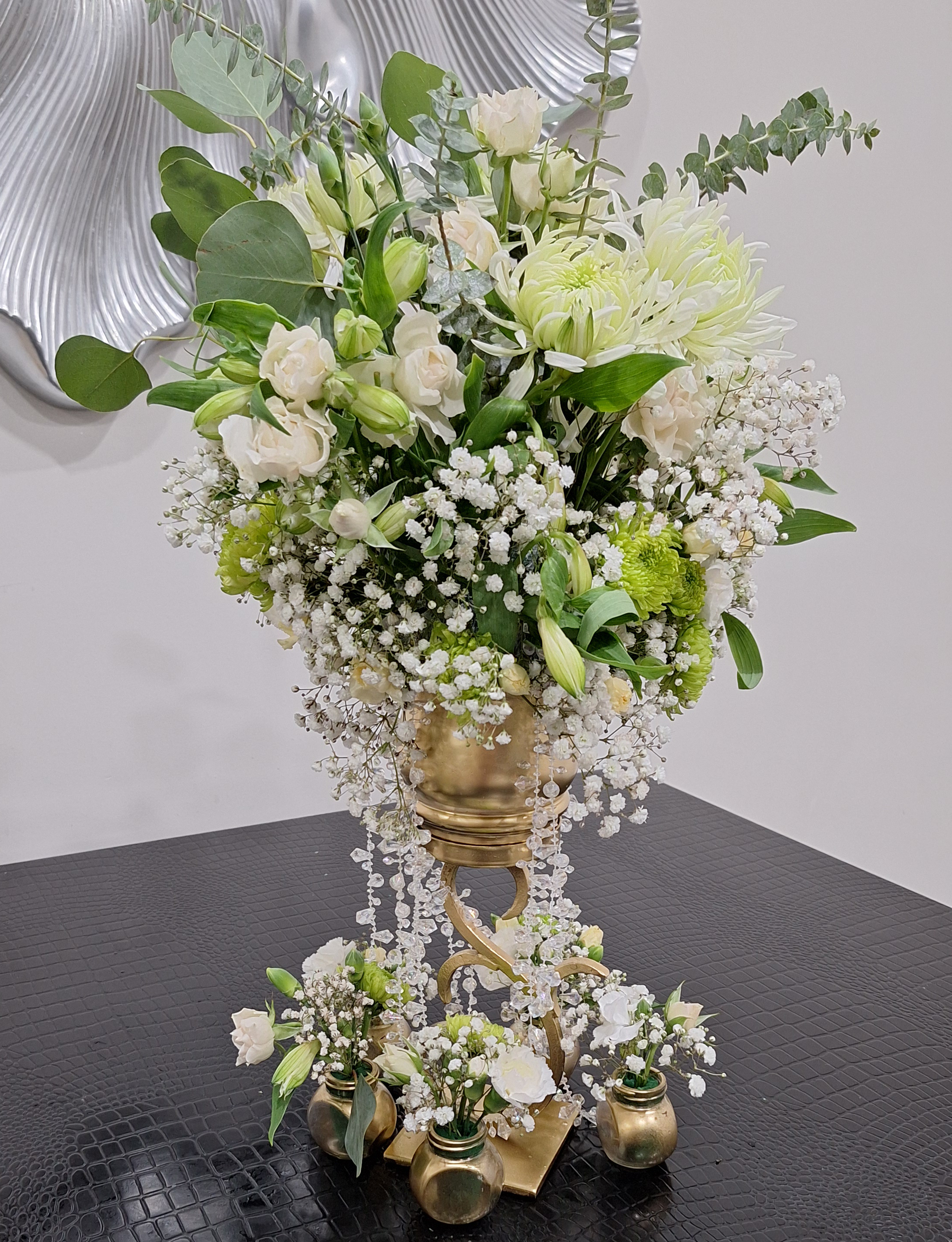 Cascading white and green floral arrangement with roses, chrysanthemums, and eucalyptus in a gold vase with crystal strands and mini vases.