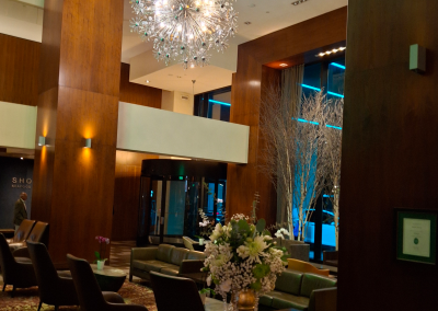 A luxurious hotel lobby with sparkling chandeliers and a white and green floral arrangement displayed on a wooden table, adding elegance to the sophisticated space.