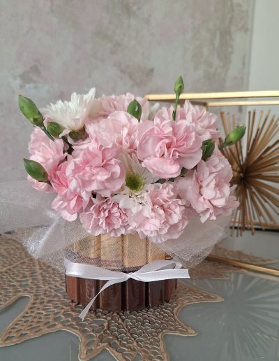 Soft pink carnations arranged with green buds, tied with a white ribbon and placed on a decorative golden leaf-patterned mat