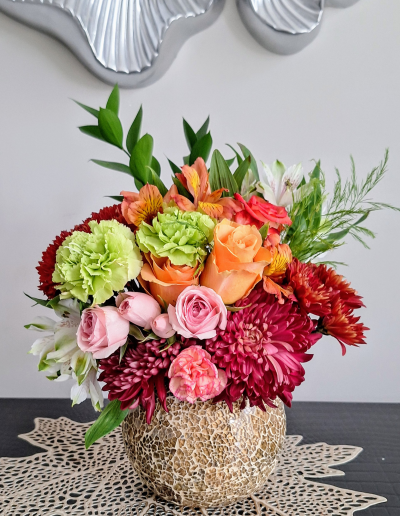 A vibrant flower arrangement in a textured ceramic vase, showcasing a mix of roses, carnations, and chrysanthemums.