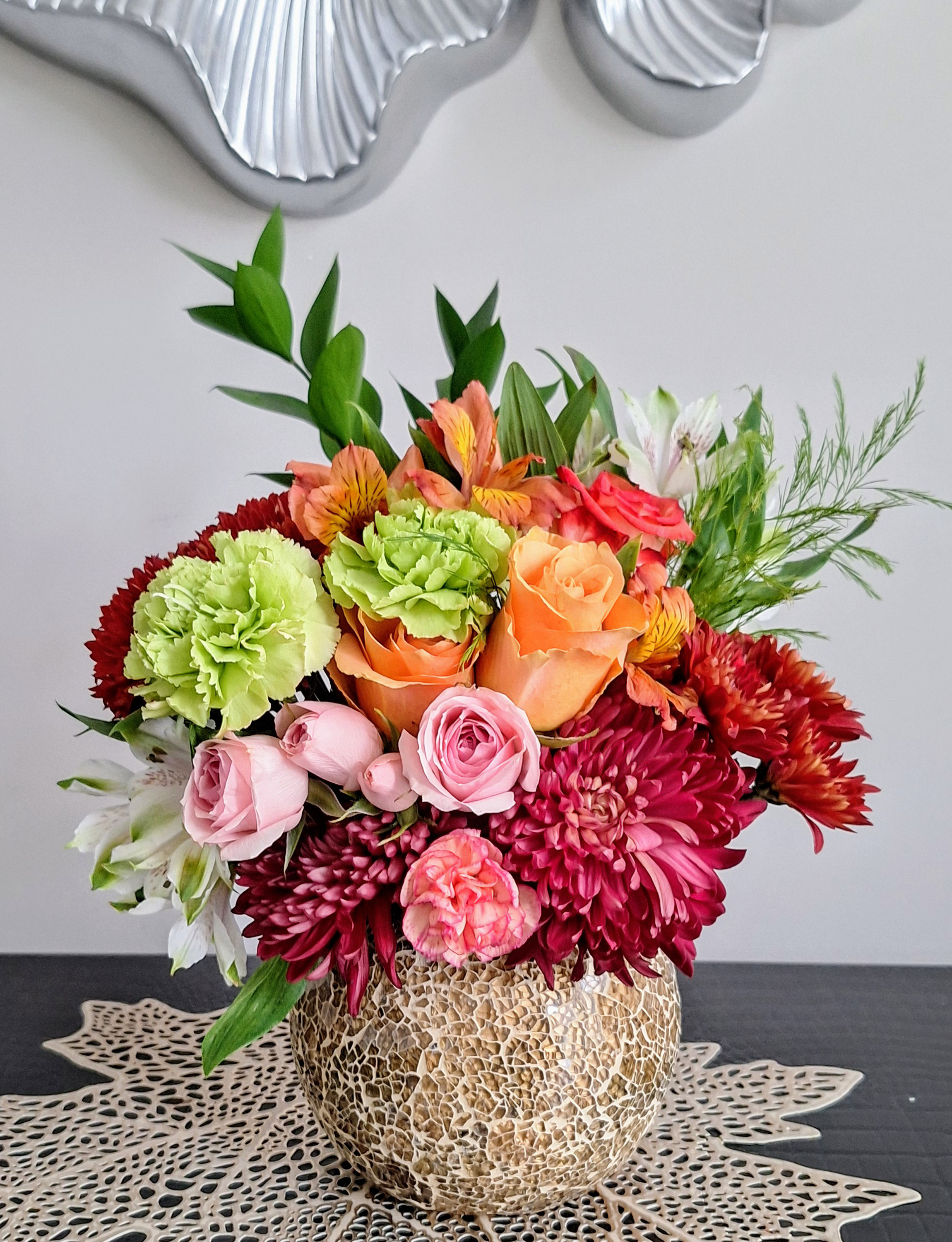 A vibrant flower arrangement in a textured ceramic vase, showcasing a mix of roses, carnations, and chrysanthemums.