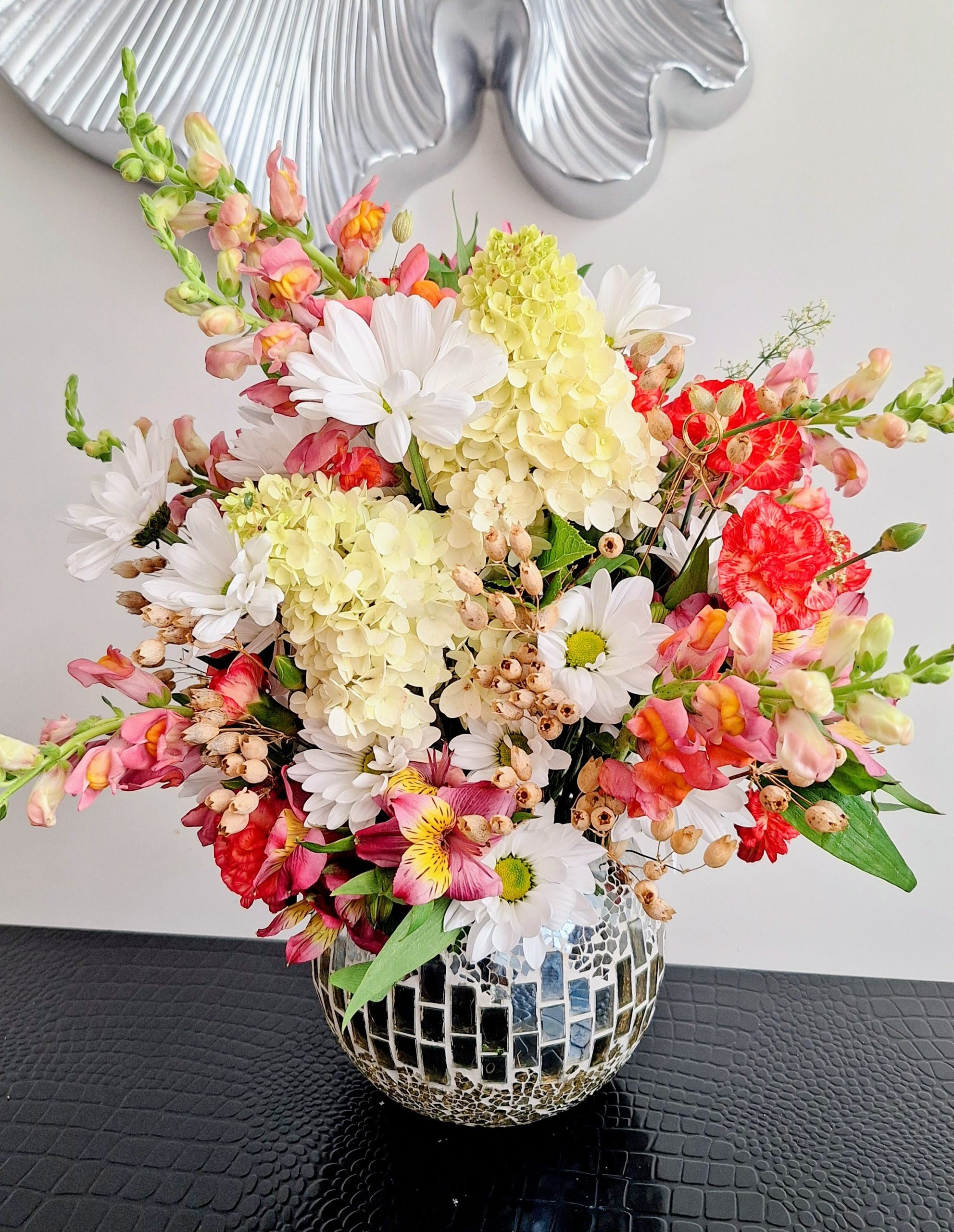 A vibrant flower arrangement in a textured ceramic vase, showcasing a mix of roses, carnations, and chrysanthemums.