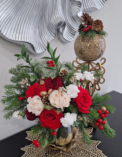 Holiday floral arrangement with red roses, pinecones, evergreen branches, and berries