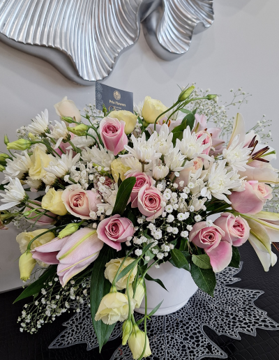 Elegant pink and white floral arrangement in a white vase with lilies and roses.
