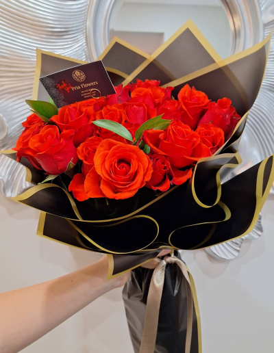 Handheld red rose bouquet wrapped in black and gold paper.