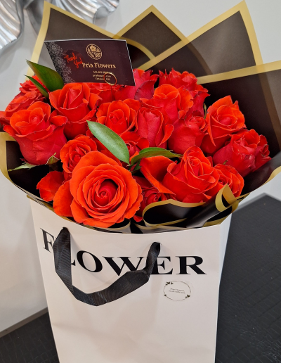 Red rose bouquet presented in a white gift bag with black and gold wrapping.
