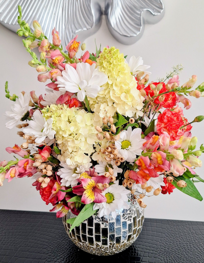Elegant mixed flower arrangement with hydrangeas, daisies, snapdragons, and seasonal blooms in a decorative mosaic vase.