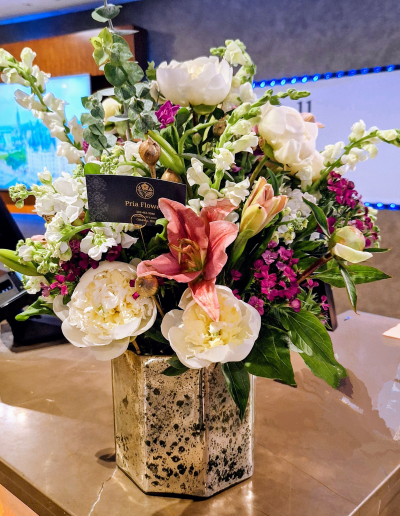 Elegant mixed flower arrangement with white peonies, pink lilies, snapdragons, and seasonal flowers in a decorative vase.