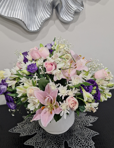 Elegant flower arrangement with pink lilies, roses, purple lisianthus, white chrysanthemums, and baby's breath in a white vase.