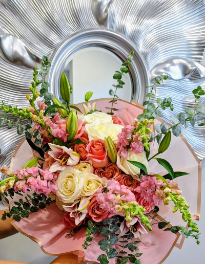 Pink and white rose bouquet with lilies and greenery wrapped in elegant pink floral paper.