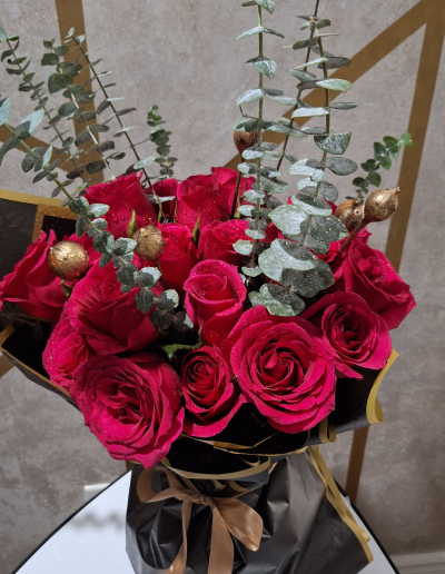 Elegant red rose bouquet with eucalyptus greenery wrapped in black and gold floral paper.