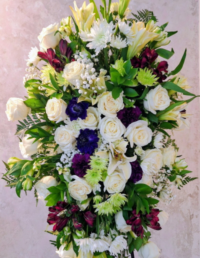 A lush floral arrangement with white roses, lilies, chrysanthemums, purple flowers, and green foliage.