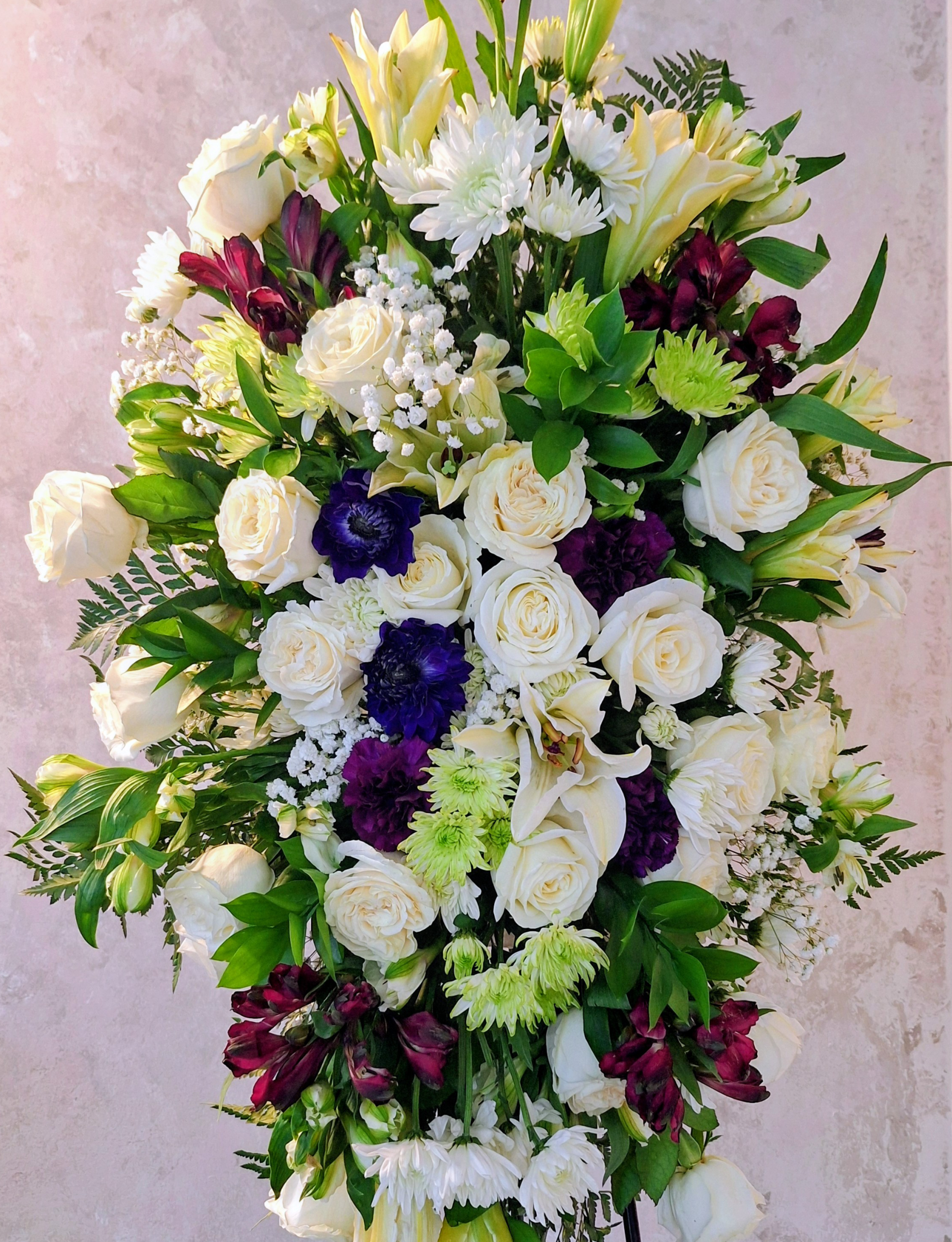 A lush floral arrangement with white roses, lilies, chrysanthemums, purple flowers, and green foliage.